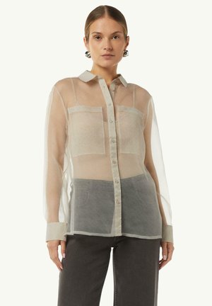 Sheer long-sleeve shirt with a light beige color, two front pockets, cream collar, and button closure, paired with dark gray pants.