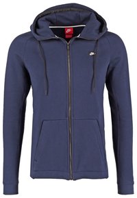 Tmavě modrá mikina s kapucí na zip z bavlněné směsi. Má kapuci se stahovací šňůrkou, přední kapsy a malou nášivku na hrudi. Hladká textura.