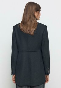 Blazer in misto lana nera con vestibilità sartoriale, spalle strutturate e polsini a tre bottoni. Presenta un design posteriore pulito e un taglio di lunghezza media.