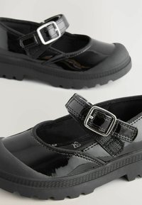 Schwarze Lackleder-Mary-Jane-Schuhe mit einem Riemen und einer silbernen Schnalle, ausgestattet mit einer strukturierten Gummisohle und einem runden Zehendesign.
