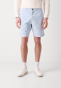 Calções de algodão azul claro com fecho de botão, bolsos laterais e um corte reto, combinados com ténis brancos e meias até ao tornozelo.