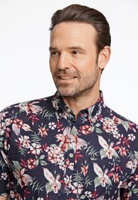 Camicia a maniche corte di colore blu navy con un motivo floreale che presenta fiori rosa e bianchi, colletto con bottoni e dettaglio della tasca sul petto.