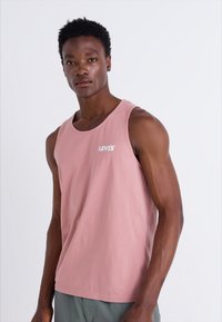 Rózsaszín pamut ujjatlan póló, kerek nyakkivágással, bal mellrészen fehér "LEVI'S" logóval. Egyszerű dizájn, minta vagy kiegészítők nélkül.