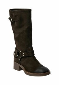 Bota de ante marrón oscuro hasta la rodilla con punta redonda, tacón y correa en el tobillo con detalles de metal plateado. Textura suave con acentos en contraste.