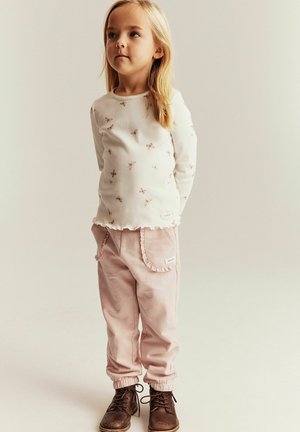 Hvid ribstrikket langærmet skjorte med blomsterprint; lyserøde bukser med flæse- lommer; brune snørestøvler.