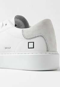 Sneaker bianca in pelle liscia, con accento in suede grigio sul tallone e dettaglio del logo nero. Presenta lacci rotondi e una suola in gomma spessa.