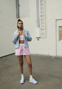 Ljusgrå kabelstickad tröja, vit kort topp, rosa randiga shorts och blå sportskor med gula detaljer. Inomhusmiljö med vita väggar.