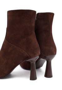 Stivaletti alla caviglia in suede marrone con un design elegante, caratterizzati da una punta arrotondata e un tacco a stiletto stretto. Chiusura con zip sul lato.