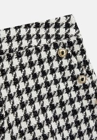 Tessuto in panno bianco e nero a motivo houndstooth con texture tessuta e bottoni in tonalità dorata sui fianchi.