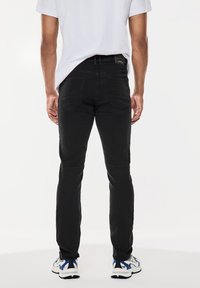 Svarta tapered jeans med en slät textur, med bakfickor och en märkning på midjan. Kommer med vita och blåa sportskor.