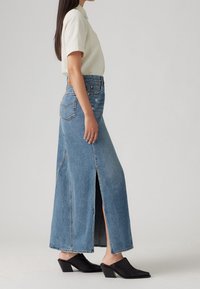 Denim maxikjol med framfickor, ljusblå färg, hög midja, fransig nederkant, kombinerad med svarta klackskor med blockh äl.