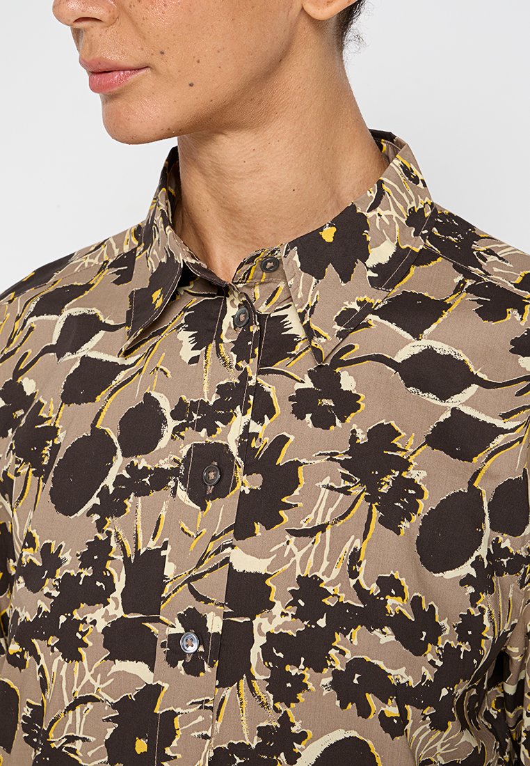 Braun gemustertes Hemd mit floralen Motiven und gelben Akzenten. Mit Kragen, Knopfverschluss und strukturiertem Stoff. Nahaufnahme des Halsauschnitts.