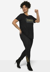 Camiseta negra con la palabra "MAGIC" en purpurina dorada, combinada con leggings de mezclilla oscuros que presentan acentos dorados en el tobillo. Botines negros de tacón.