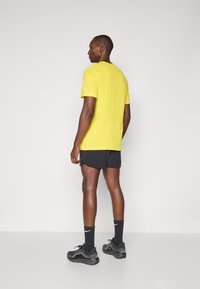 Gul t-shirt med kort ärm och rund halsringning, kombinerad med svarta träningsshorts. Avslutad med svarta strumpor och grå löparskor.