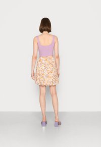 Top cropped em lilás com textura, combinado com uma saia mini em padrão de leopardo nas tonalidades de laranja e amarelo. Faixa elástica branca na cintura, mules com salto bloco.