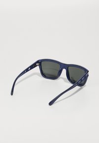 Óculos de sol azuis com uma armação texturizada distinta, lentes escuras e uma forma angulada. As características incluem braços finos e alongados.