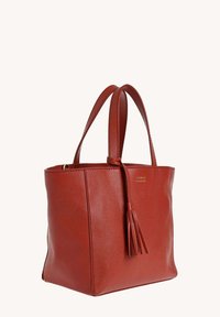 Sac cabas en cuir rouge avec double poignées et un détail de frange à l'avant, texture douce et granuleuse, portant debout sur un fond blanc.