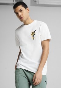 Hvid bomulds T-shirt med korte ærmer, der har et sort og guld grafisk design på brystet og en rund halsudskæring.