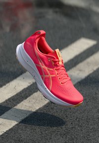 Running shoe with a bright pink upper, textured design, and golden accents. Features cushioned sole and rounded toe for support.