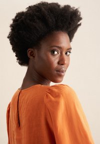 Blusa in lino arancione con maniche a sbuffo e dettaglio a chiave sul retro, caratterizzata da una texture morbida e una silhouette rilassata.
