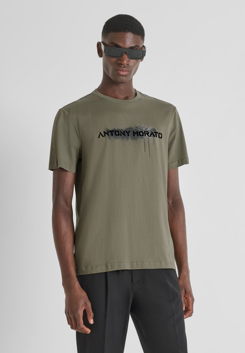 Camiseta de algodón verde oliva con mangas cortas y cuello redondo, con el texto impreso en negro "ANTONY MORATO" y un diseño de efecto salpicado.