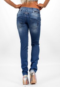 Jeans blu slim fit con una finitura sbiadita, cinque tasche, cuciture a contrasto e un paio di scarpe col tacco alto lucide e multicolori.