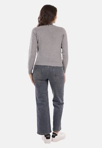 Maglione grigio a maglia con maniche aderenti, abbinato a jeans blu a vita alta e sneaker bianche con dettagli neri. Design semplice, senza motivi.