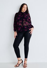 Blouse noire transparente avec un motif floral rose, design à boutons, associée à un legging en cuir noir et des escarpins noirs à lanières.