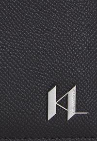 Juodas tekstūruotas oda su sidabriniu logotipu, kuriame įrašyta "KL" ir "KARL LAGERFELD". Kompaktiškas ir rafinuotas dizainas.