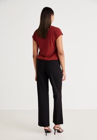 Rode top met korte mouwen in een ontspannen pasvorm, gecombineerd met zwarte wijde broek en zwarte strappy hakken, gezien van achteren. Glad textuur.