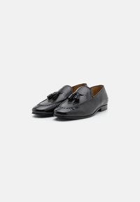 Mocasini din piele neagră cu un finisaj lucios, având un design cu decupaj, cu două ciucuri în față și un toc jos.