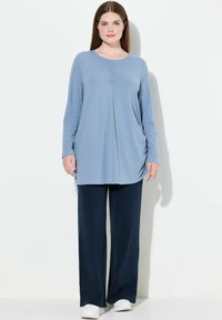 Maglione a maniche lunghe azzurro chiaro con arricciatura frontale, abbinato a pantaloni blu navy dalla vestibilità ampia. Modello con scarpe bianche. Design semplice e informale.