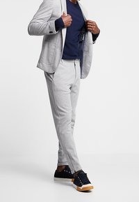 Szary dzianinowy żakiet w zestawie z pasującymi szarymi spodniami. Do tego granatowy top i czarne trampki z białą podeszwą i pomarańczowymi akcentami.