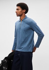 Meeste pikkade varrukatega polosärk pehmes sinises kangas, zippkraega, peene logodetaili ja sirge lõikega.