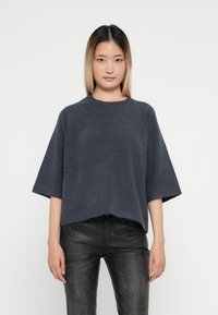 Mörkgrå stickad oversized tröja med rund halsringning och vida ärmar, matchad med svarta texturerade byxor.