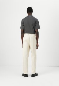 Chemise gris foncé à manches courtes et pantalon crème, avec une coupe droite et un design minimaliste, vue de derrière. Des chaussures noires sont portées.