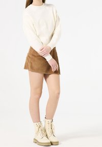 Krämfärgad stickad tröja med ribbad textur, kombinerad med en brun kordfläck mini kjol. Skorna är beige snörboots med guld detaljer.