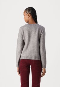 Suéter gris de punto con cuello redondo, dobladillo acanalado y mangas largas, combinado con pantalones de pana burdeos. Acabado de tela texturizada.