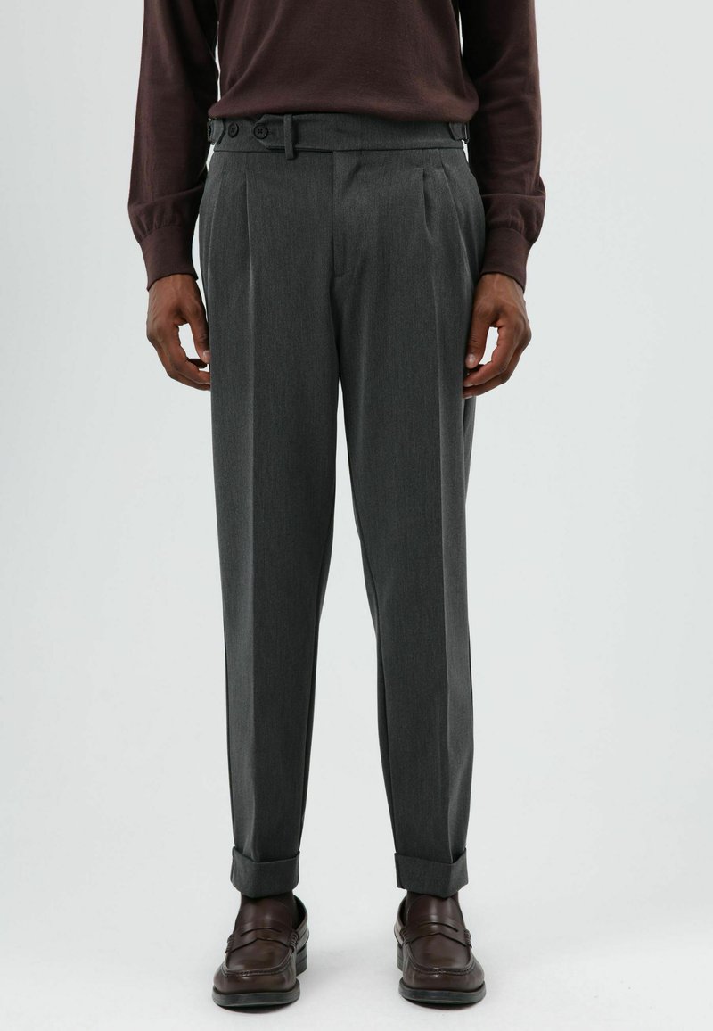 Grijze geplooide pantalon met taps toelopend ontwerp, gemaakt van getextureerde stof, voorzien van een riem met knopen en omgeslagen manchet. Gemonteerd met bruine schoenen.