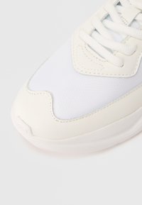 Close-up of white sneaker toe with mesh and leather upper and white laces on a plain background.