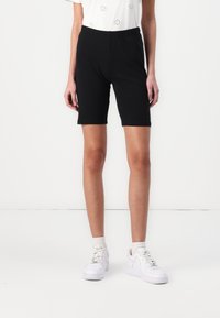 Black bike shorts made of stretchy fabric, featuring an elastic waistband. Paired with a white embroidered top and white sneakers.