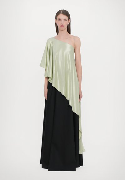 Vestido asimétrico en satén verde claro con una manga corta, detalle drapeado, combinado con una falda larga negra, con forma fluida y textura suave.