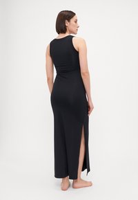 Abito maxi nero realizzato in tessuto elastico, caratterizzato da un design senza maniche e uno spacco laterale, con un corpo aderente e una gonna lunga.