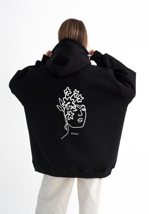 Zwarte oversized hoodie van katoen. Heeft een witte lijntekening van een gezicht met bloemaccenten op de achterkant. Met capuchon.