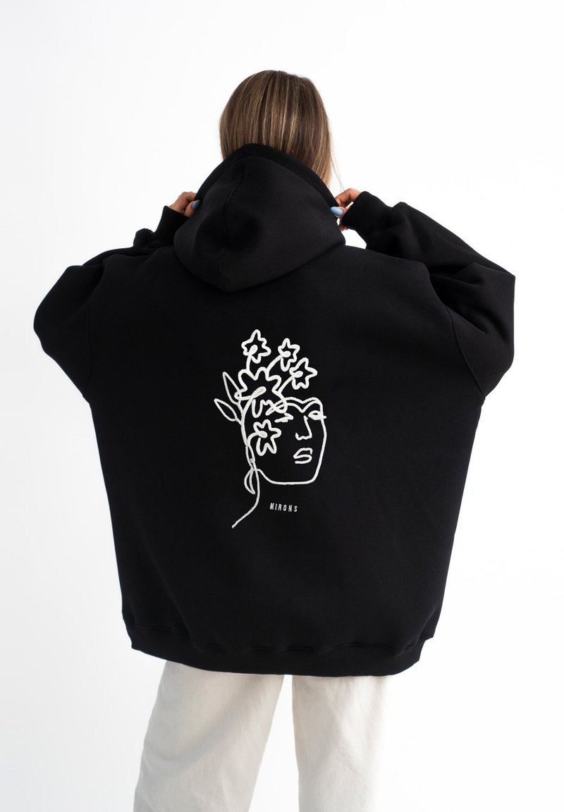 Felpa nera oversize in cotone. Presenta un design di arte lineare bianca di un volto con accenti floreali sulla schiena. Cappuccio attaccato.