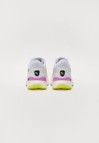 Witte sportschoenen met een gestructureerde bovenkant, voorzien van paarse en gele accenten op de zool, een zwart logo op de hiel en een gevoerd ontwerp.