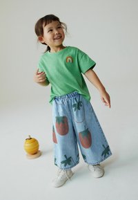 Grøn T-shirt med korte ærmer og en regnbuepatch, kombineret med vidde denimbukser med røde jordbærmønstre og elastik i taljen.