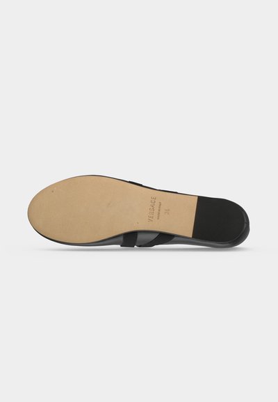Semelle d'une chaussure en cuir noire avec une semelle beige, comportant la marque Versace et la taille 34.