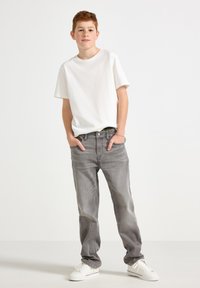 Jean en denim gris avec une coupe droite, associé à un t-shirt blanc simple et des baskets blanches. Les jeans disposent d'une fermeture à bouton et de poches avant.