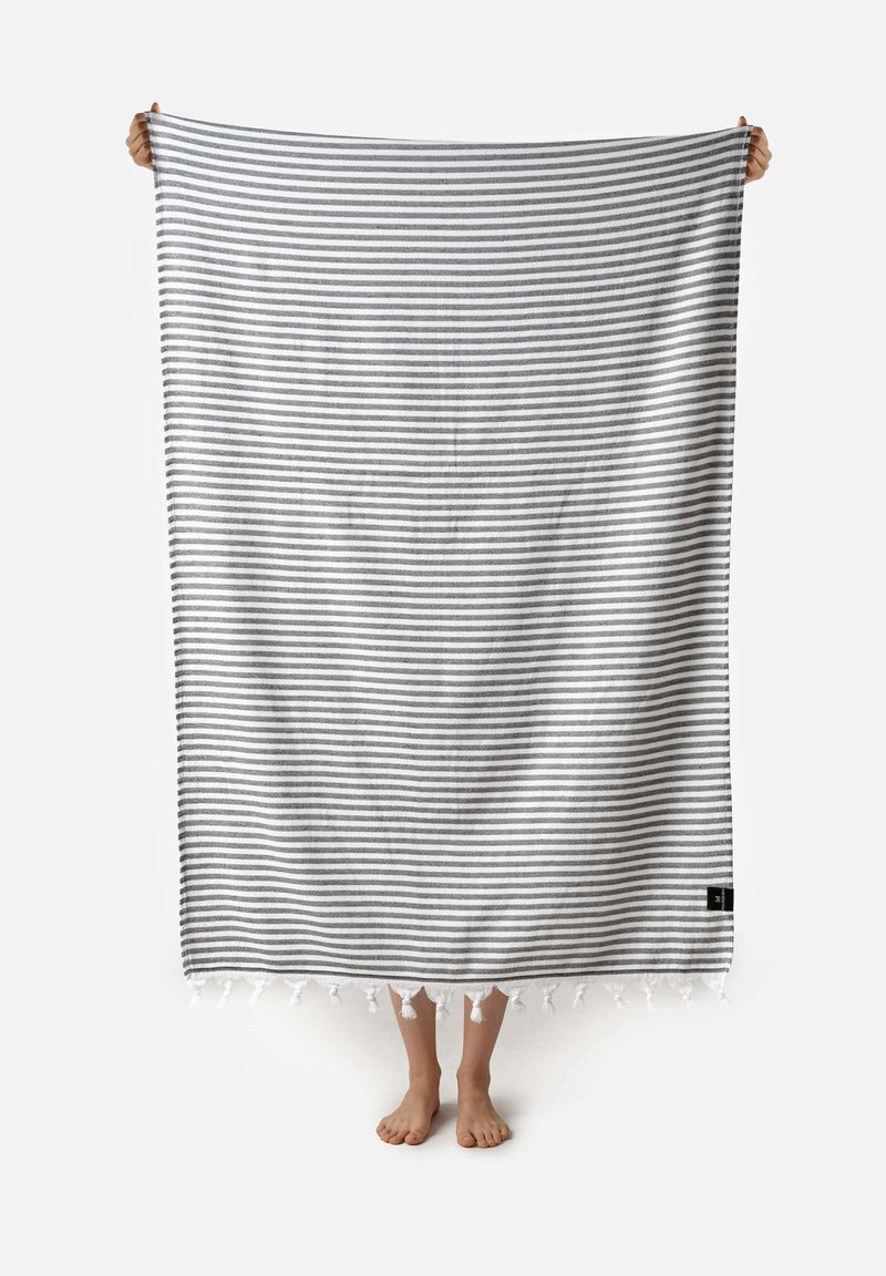 Manta de algodón a rayas en gris y blanco, con flecos en los extremos; sostenida por una persona, mostrando toda su longitud y textura.